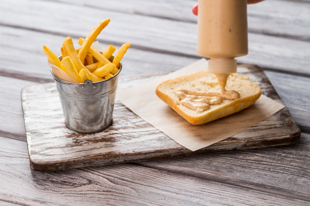 Image of putting sauce in a sandwich besides french fries. 