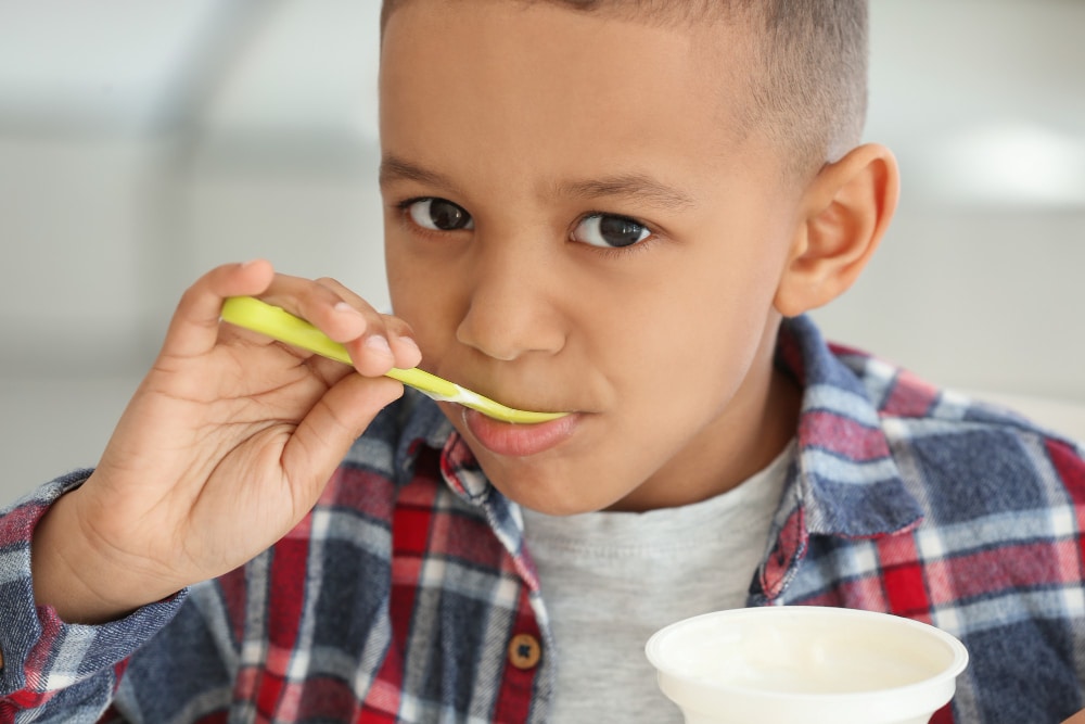 Image of a kid having a taste of yogurt in a plastic container
