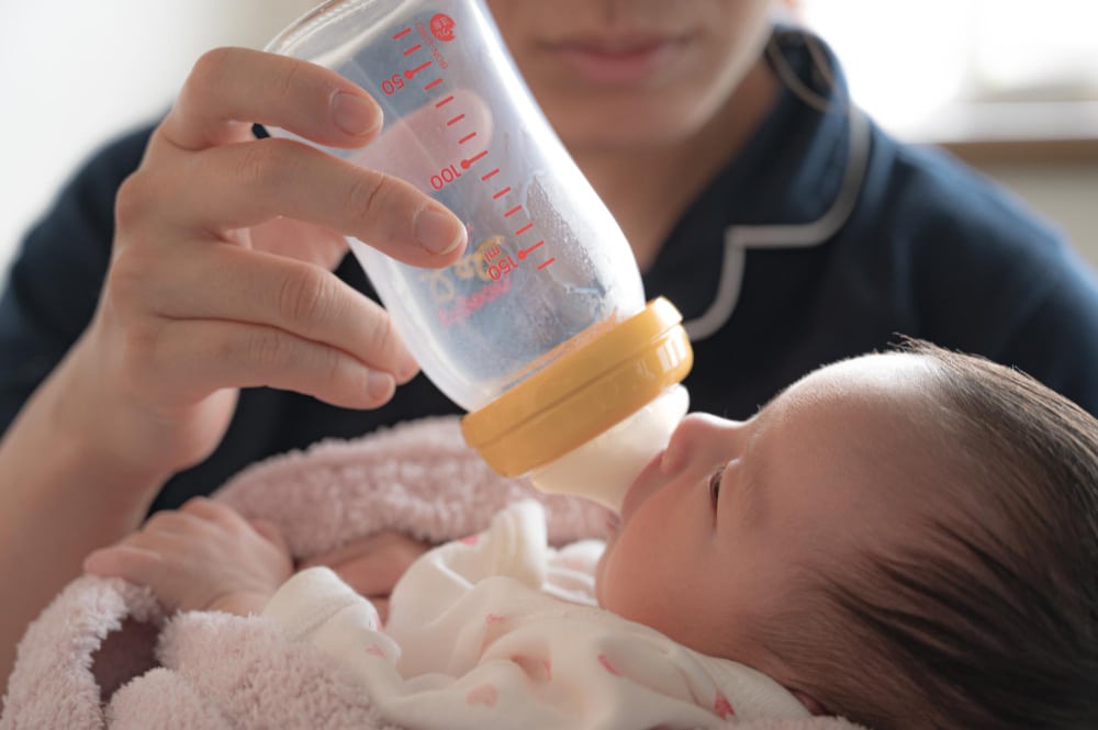 Image of a woman feeding a newborn baby with a plastic bottle