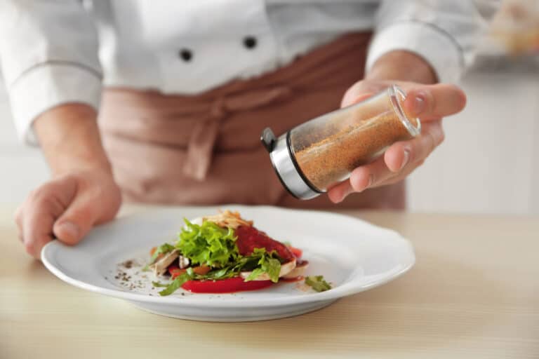 Chef cook adding pepper to dish, closeup using a condiment plastic bottles