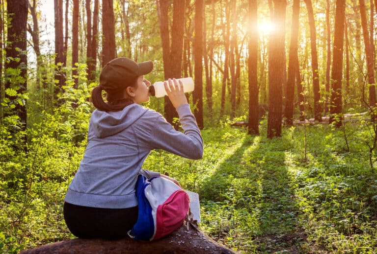 a women drinking water from a 32 oz Plastic Bottle while hiking