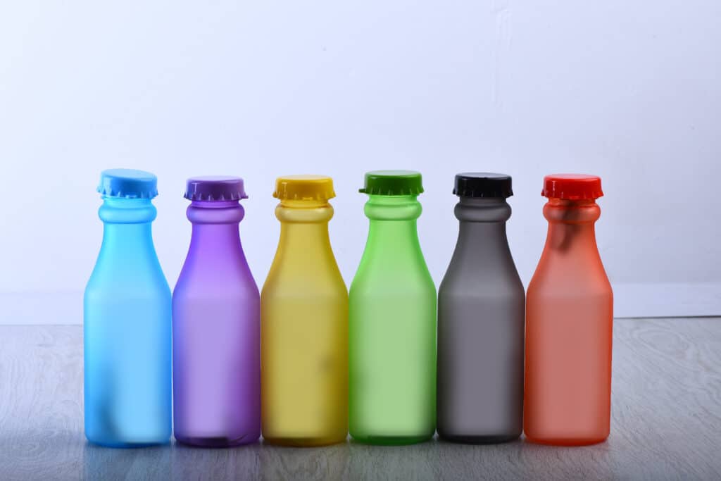 Row of colorful 12 oz Plastic Bottles with Caps on grey background background. Energy drinks containers with various flavors on wooden table. Colour choice and containers concept. Set of bottles in different color.