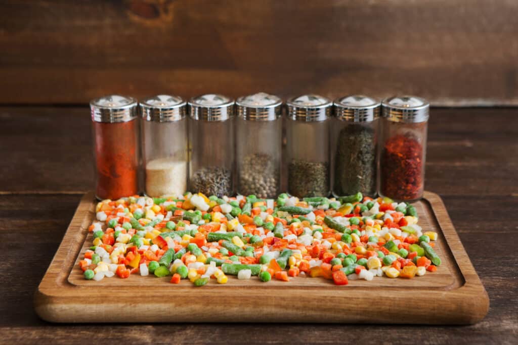 Spices and frozen vegetables on cutting board. Meal preparation, wooden backgroud, condiment plastic bottles