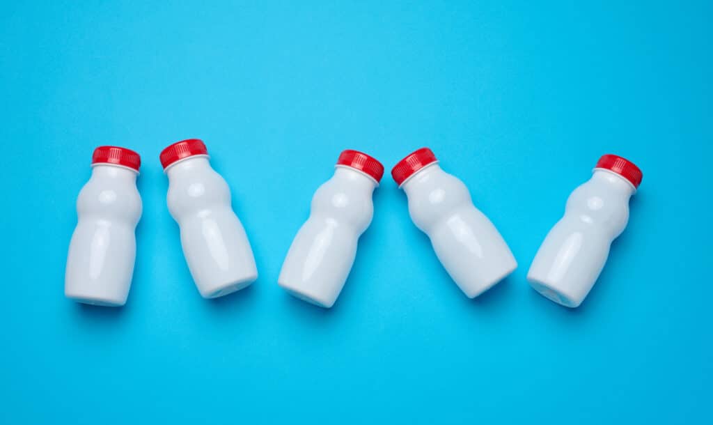 White plastic bottles with lids for dairy products on a blue background, top view