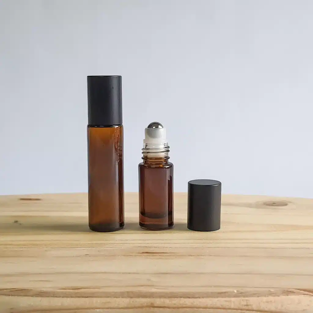 Amber glass roll-on bottle with stainless steel roller ball and black cap on a wooden table.