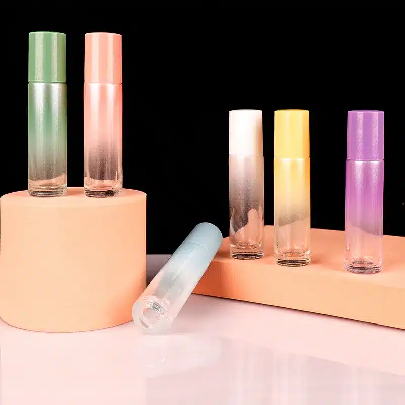 A collection of colorful glass roll-on bottles with pastel-colored caps, displayed on a peach-toned pedestal .