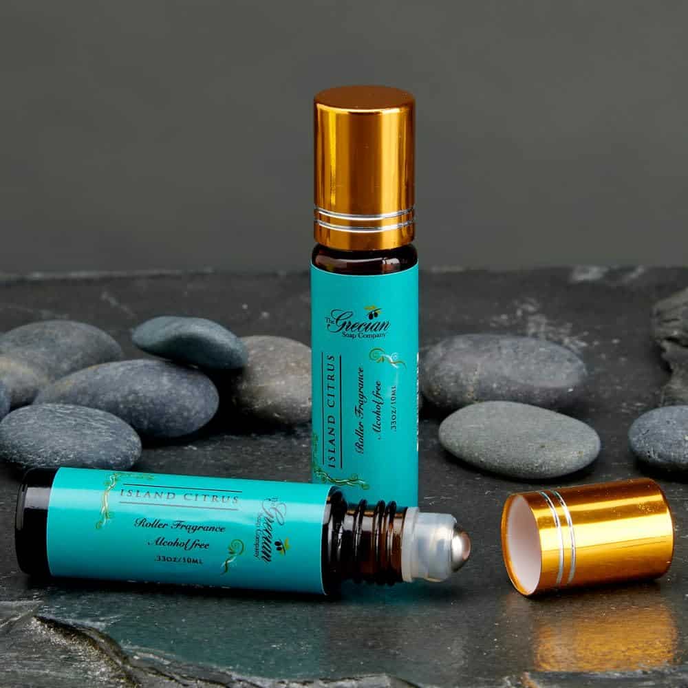 Two turquoise roll-on fragrance bottles with gold caps, one open to show the rollerball, on a dark background with pebbles.