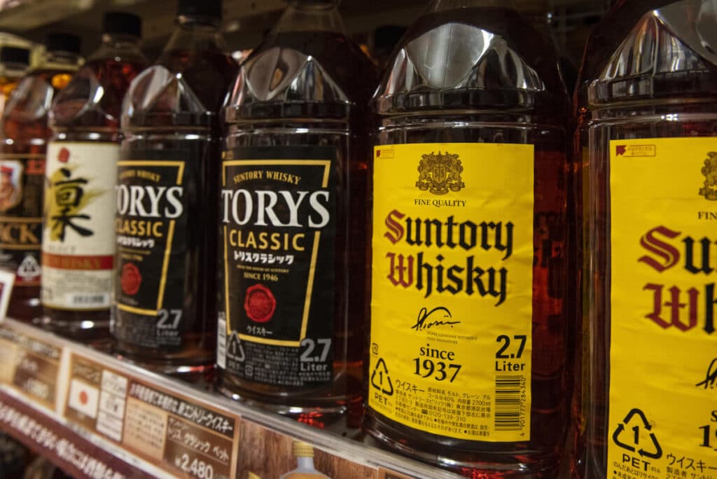 Several large Suntory Whisky stored in plastic bottles for liquor, lined up on a store shelf. 