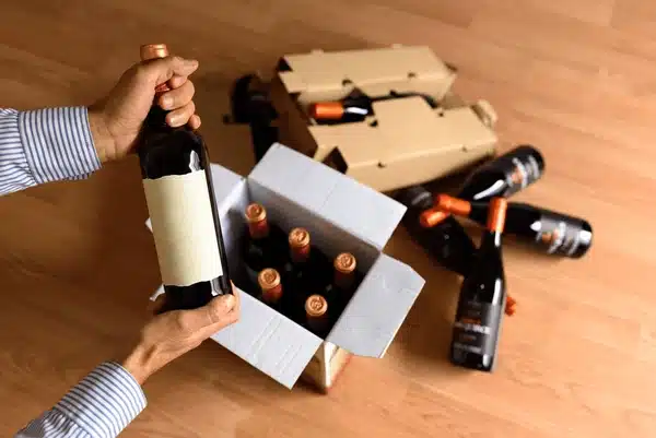 Hands placing a wine bottle into a cardboard box with other wine bottles.