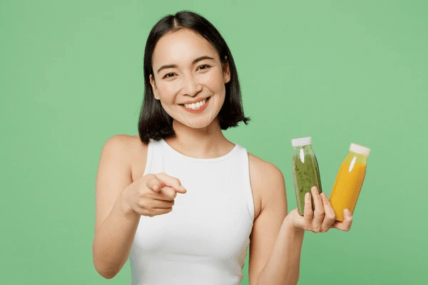 A smiling woman holding two plastic juice containers in one hand and pointing the other hand. 