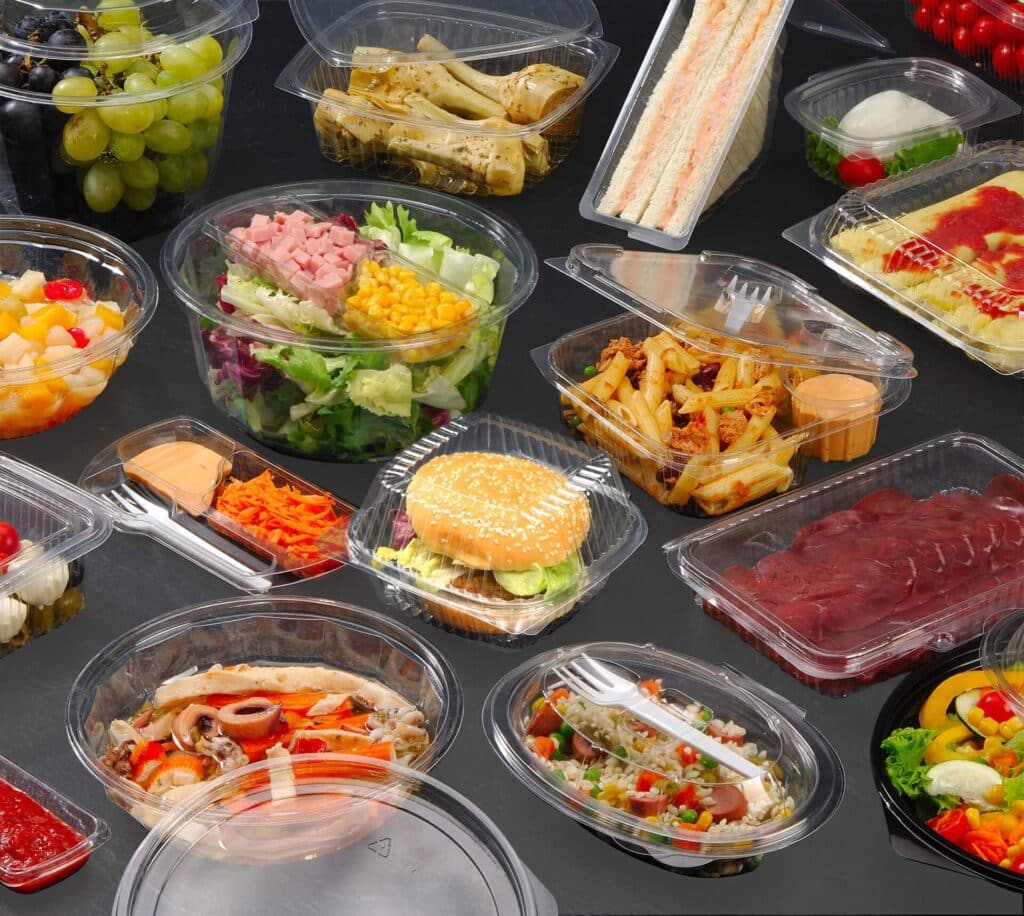 A variety of prepared foods packaged in plastic containers- including pasta, burger, salads, fruits, and sandwiches. 