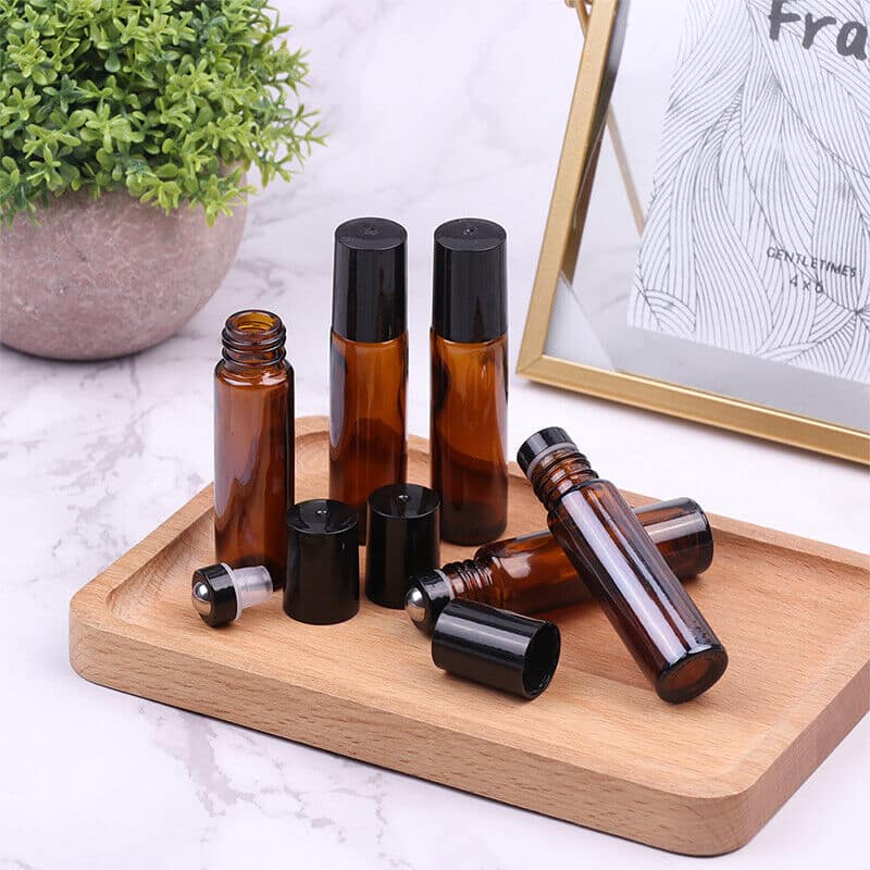 Amber glass roll-on bottles with black caps and stainless steel roller balls on a wooden tray.