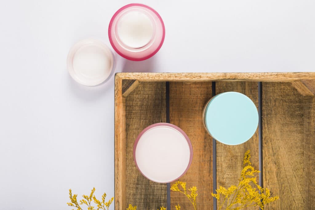 plastic cosmetics jars kept on a wooden tray that kept on a white backgound 