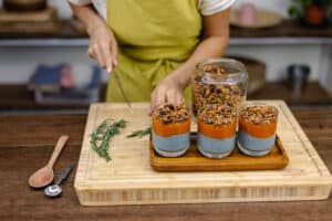 woman-with-colorful-healthy-sweet-deserts-chia-puddings-made-almond-milk-blue-spirulina-extract-chia-seeds-pappaya-mango-jam-homemade-granola-wooden-table-kitchen-home storing in a plastic container